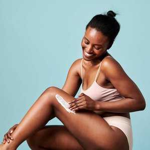 Smiling Model for Superfacialist applying moisturiser to her leg. Photographed and styled by cosmetic photographer Tom Hargreaves in his studio in Exeter, Devon
