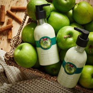 The Bodyshop spiced apple softening body lotion lying in a basket of apples. Photographed and styled by cosmetic photographer Tom Hargreaves in his studio in Exeter, Devon
