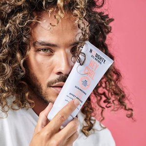 portrait of Curly haired male model holding Noughty Haircare Hey Curl Scrunching Jelly.
Photographed by Tom Hargreaves in a London studio.