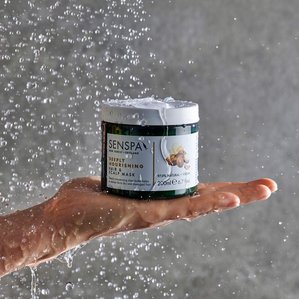 Senspa deeply nourishing hair &amp;amp;amp; scalp mask in a shower setting on palm of models hand with shower water dripping onto product and hand. Photographed and styled by cosmetic photographer Tom Hargreaves in his studio in Exeter, Devon