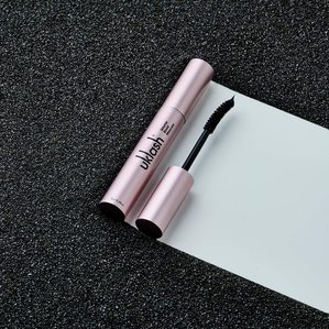 Uklash volume boost mascara lying on black sand. Photographed and styled by cosmetic photographer Tom Hargreaves in his studio in Exeter, Devon