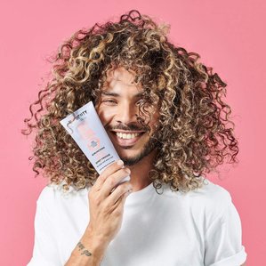 Male curly haired model holding Noughty haircare Hey Curl scrunching Jelly.
Photographed and styled by Tom Hargreaves in a London studio