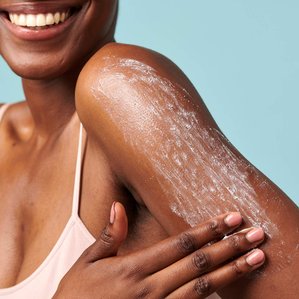 Smiling Model for Superfacialist applying body scrub to her arm. Photographed and styled by cosmetic photographer Tom Hargreaves in his studio in Exeter, Devon