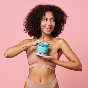 Smiling curly haired model holding Dirty works buttery salt scrub. Photographed and styled by cosmetic photographer Tom Hargreaves in his studio in Exeter, Devon