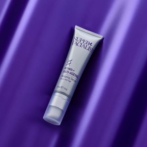 Tube of Superfacialist Retinol+ Anti Ageing Restoring Serum lying on contoured metallic purple backdrop. Photographed and styled by cosmetic photographer Tom Hargreaves in his studio in Exeter, Devon