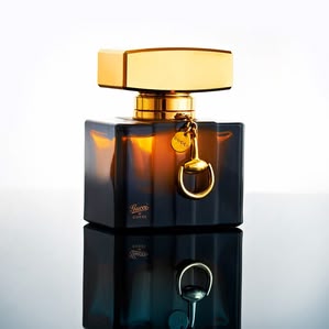 Glass Gucci perfume bottle with gold lid standing on mirror. Photographed and styled by cosmetic photographer Tom Hargreaves in his studio in Exeter, Devon