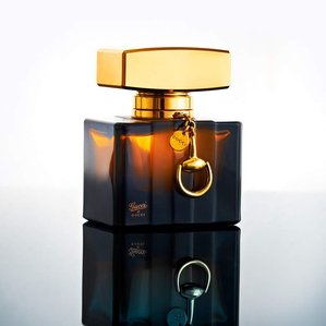 Glass Gucci perfume bottle with gold lid standing on mirror. Photographed and styled by cosmetic photographer Tom Hargreaves in his studio in Exeter, Devon