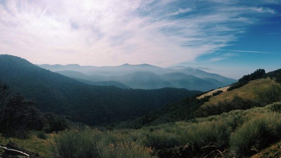 A wide, verdant vista of the Tehachapi Mountain Range under a cloudy sky. 