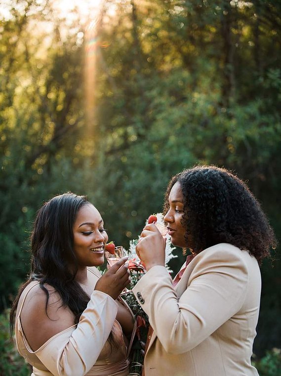 Two brides toasting to each other and their relationship with pink lemonade in champagne glasses