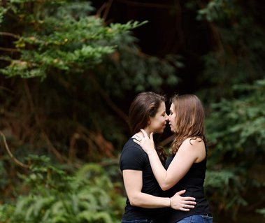 two women share an intimate embrace among the redwoods as they celebrate their engagement with an adventure photography session
