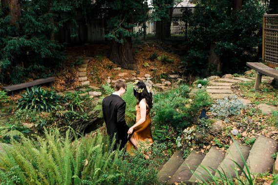 A bride and groom walk down a garden path towards a stream