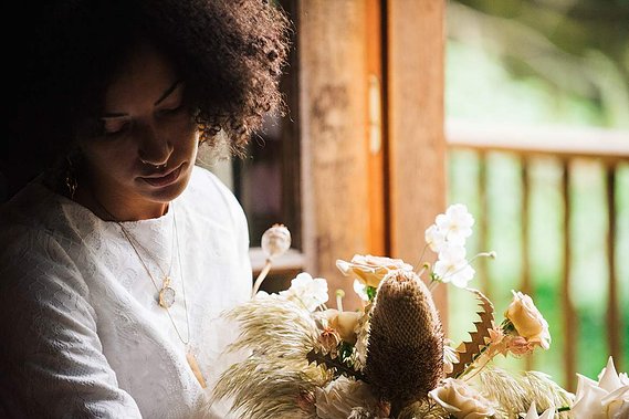 The bride sits with her bouquet by a cabin window