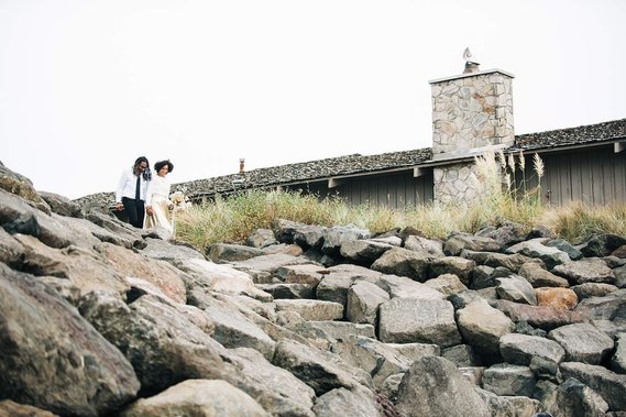 The bride and groom walk down a rocky set of steps to the beach