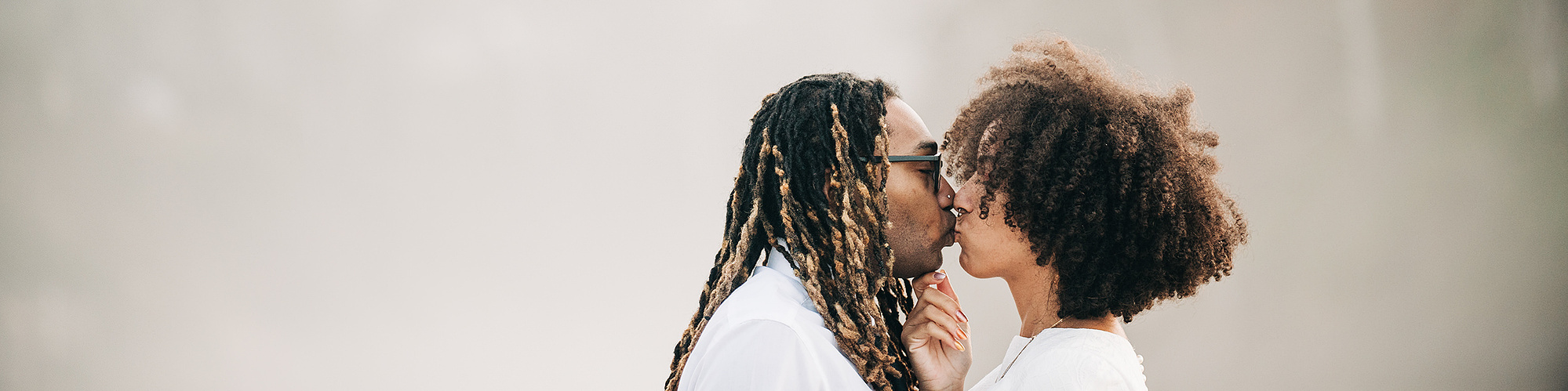 A bride and groom kiss lightly on an Oregon Coast beach, forested ridgelines rising behind them