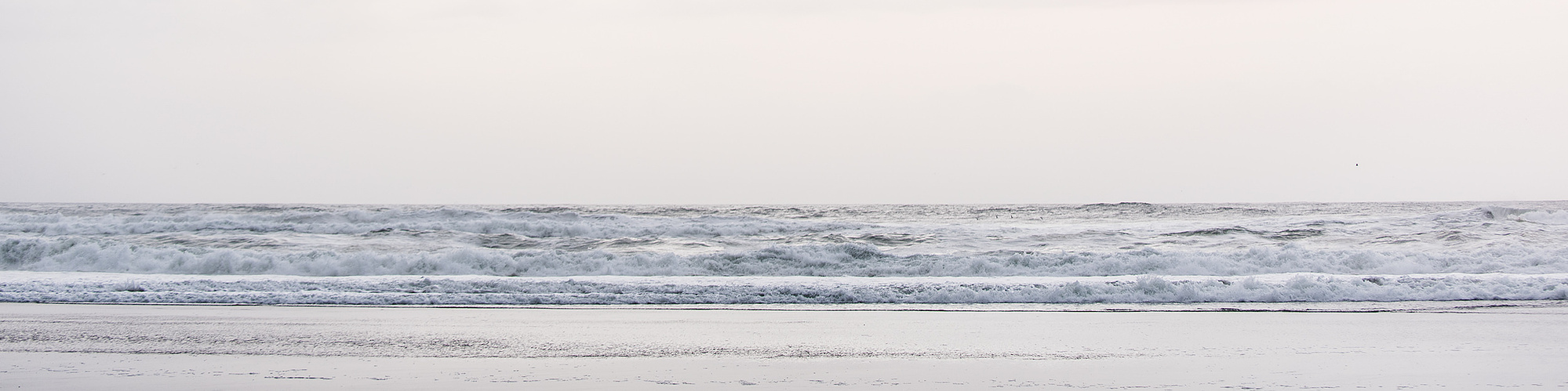 A wide, flat sea, seen from the beach and topped by a cloudy sky