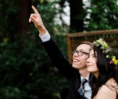 a man and woman relax in their backyard after their wedding ceremony; they both look upwards as the man points to the sky