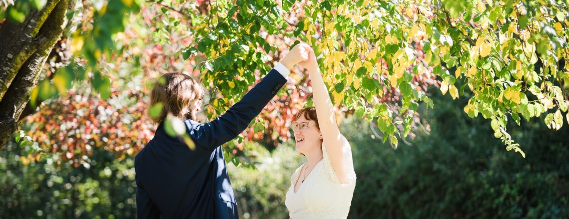 A bride a groom, both wearing glasses, dance under a tree after their elopement ceremony