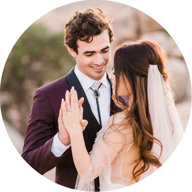 A bride and groom intertwine their fingers as they snuggle together in Joshua Tree National Park