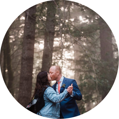 A casually-dressed bride and groom dance in a misty forest at twilight