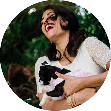 A bride in a white dress holds a puppy and laughs