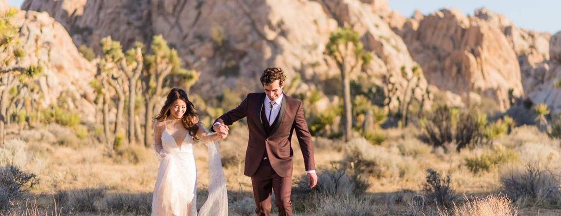 a young newlywed couple runs playfully through the desert at Joshua Tree National Park