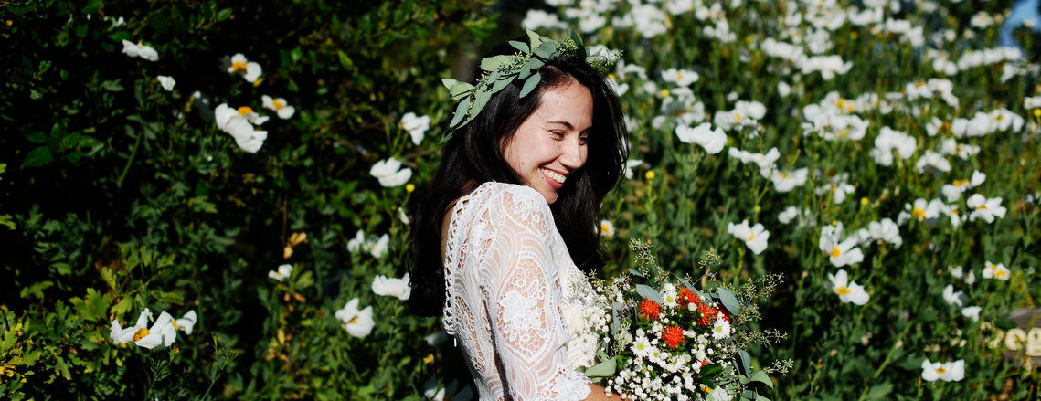 a bride giggles into her bouquet, surrounded by California wildflowers