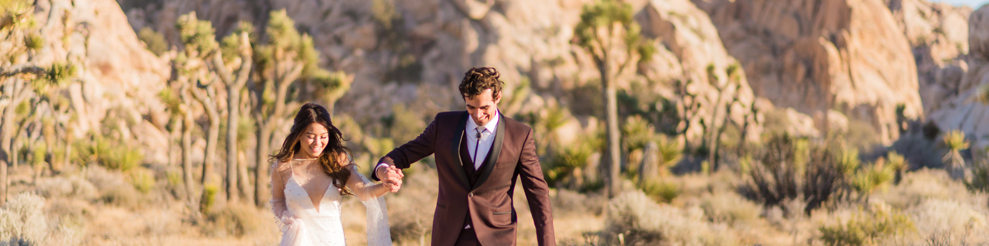 An eloping bride and groom run excitedly through the desert in Joshua Tree National Park