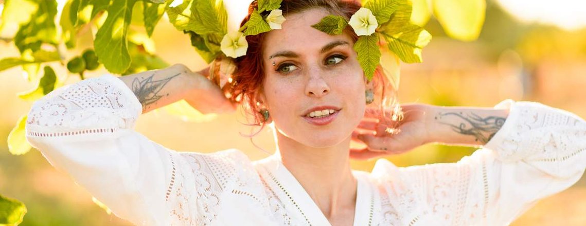 a young bride with tattoos raises her arms to her head as she feels the sunlight on the back of her neck