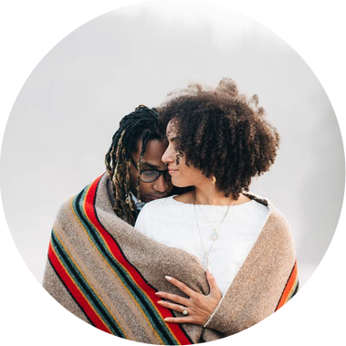 A bride and groom hug each other, wrapped in a striped wool blanket