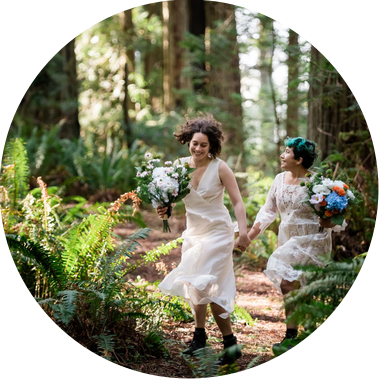 An eloping couple runs through the California redwoods, wearing matching bridal gowns