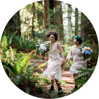 An eloping couple runs through the California redwoods, wearing matching bridal gowns