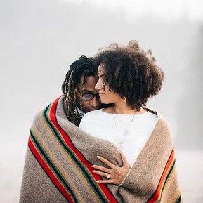 The bride and groom snuggle together under a striped wool blanket