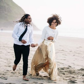 The bride and groom run together along the beach