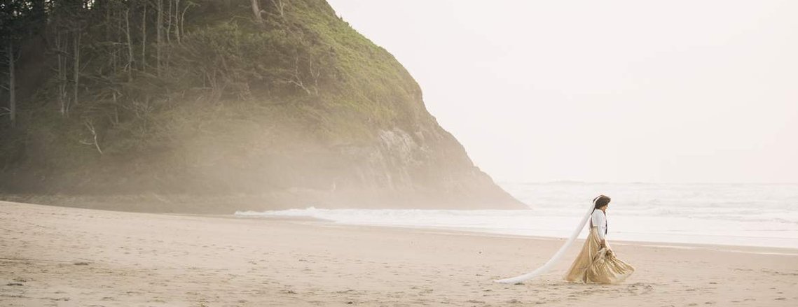 Pacific Northwest Elopement Photography Packages: A bride and groom walk along a misty beach on the Oregon Coast