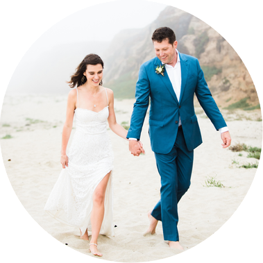 A bride and groom laugh as they walk together along a foggy beach in Half Moon Bay, California