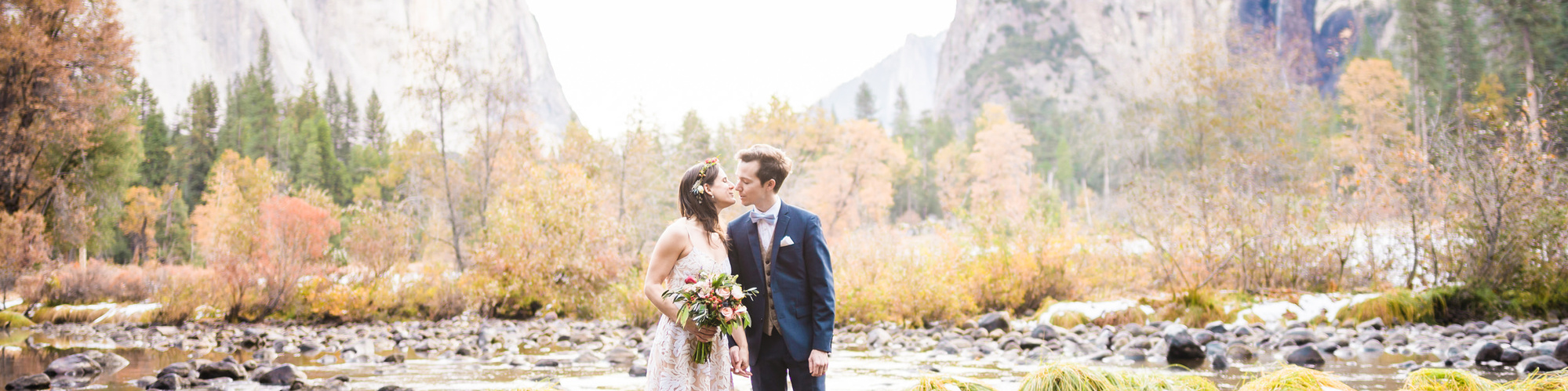 A bride and groom lean in towards each other for a sunrise kiss in Yosemite valley, the granite walls of the Valley rising behind them in the distance