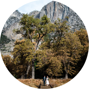 A bride and groom walk along a boardwalk in Yosemite National Park, granite cliffs towering above them