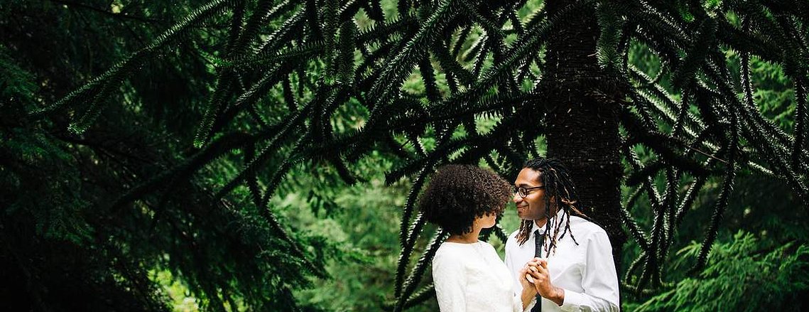 A bride and groom stand below a tall tree in a lush green Oregon foest