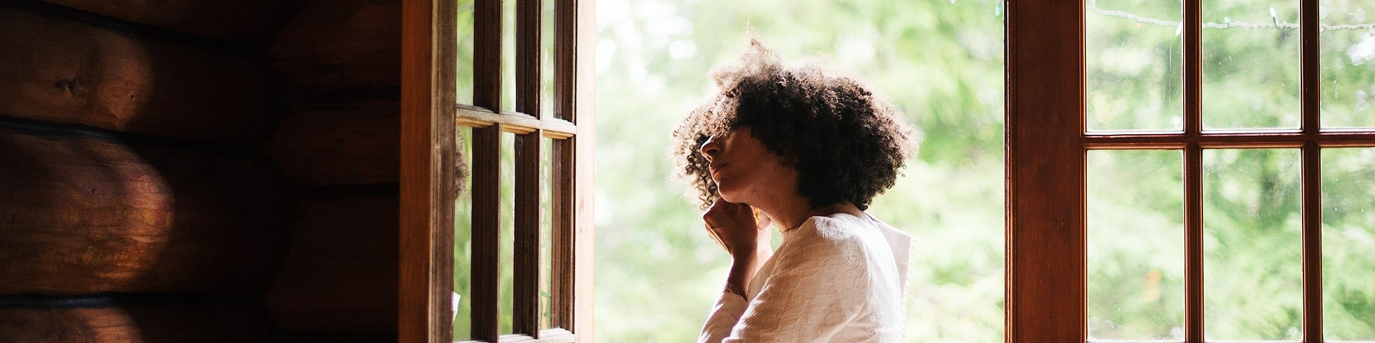 A bride stands in the doorway of a cabin in the forest, as she puts her bridal jewelry on
