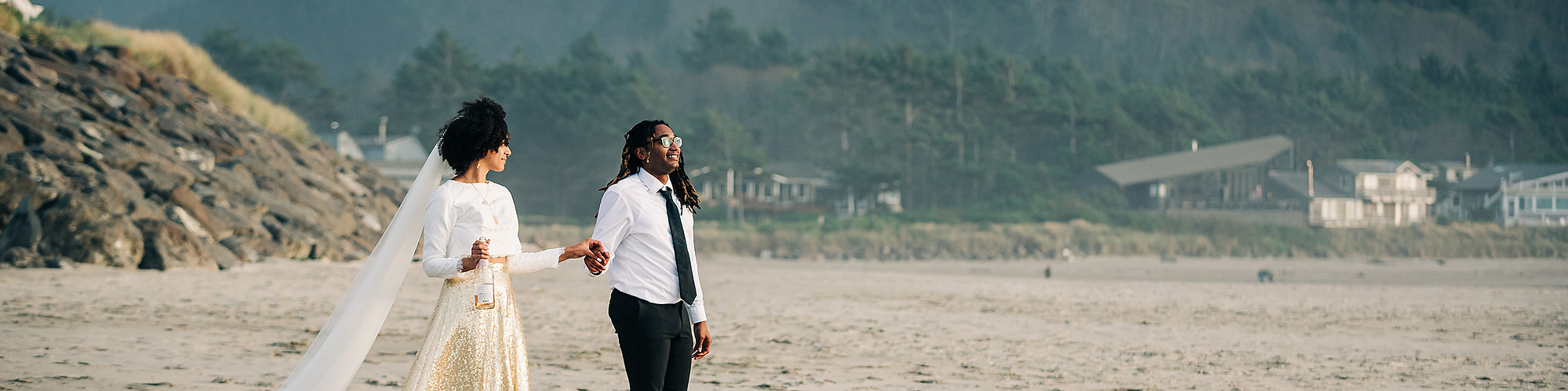 A bride and groom stroll together along a sandy beach on the Oregon Coast
