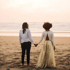 Their backs to us, the bride and groom stand side by side at the end of their elopement day, looking out at the sunset