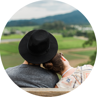 A couple sits on a park bench and gazes out at the farmland in the valley below them