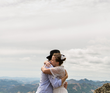 An eloping couple hugs under a dramatic cloudy sky