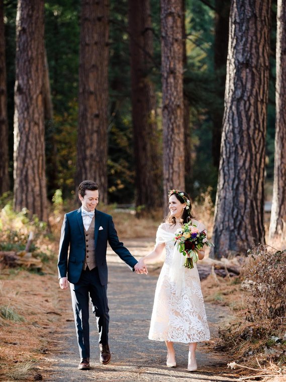 A bride and groom walk through a tall grove of trees at Yosemite National Park