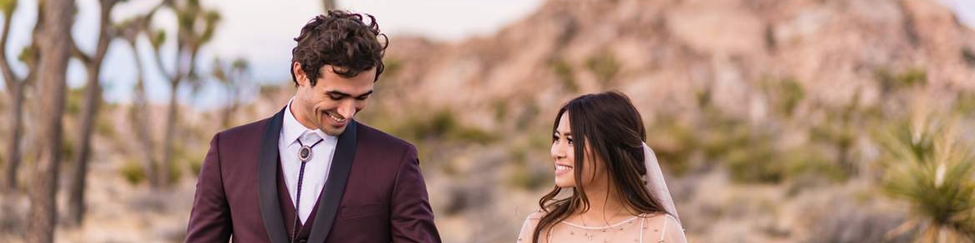 An eloping couple walks through the desert in Joshua Tree National Park, smiling