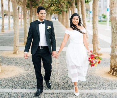 a joyful pair of newlyweds walk hand-in-hand through the park outside San Francisco City Hall after their elopement