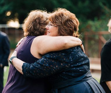 Two guests at an intimate wedding embrace in a heartfelt hug