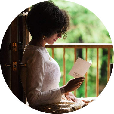 A bride sits in the doorway of a forest cabin, reading a letter written to her by her future groom