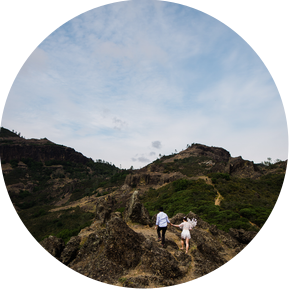 A bride and groom make their way along a rocky path in the mountains