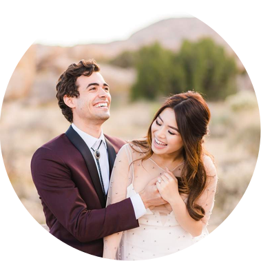 A young bride sits on her groom's lap, both laughing enthusiastically